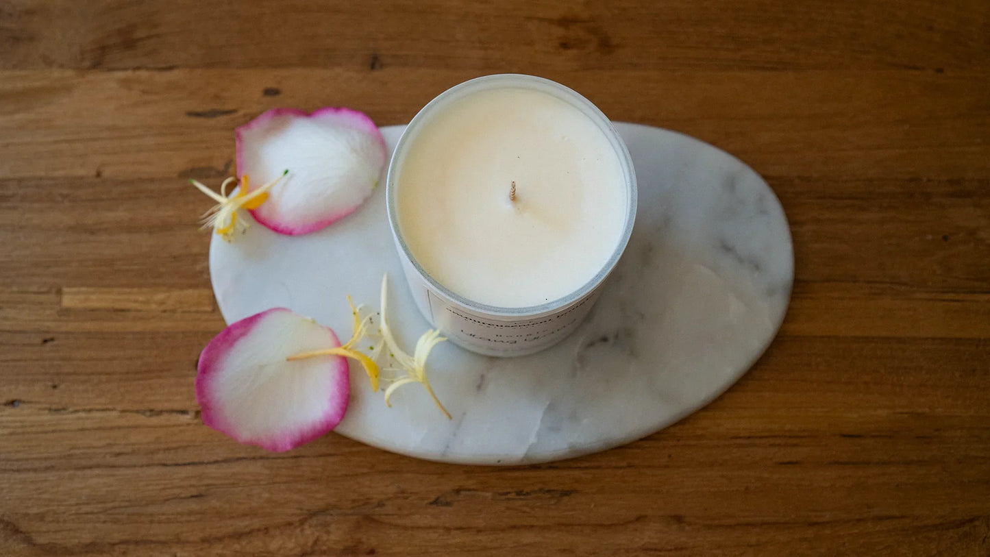 Bougie artisanale parfumée blanche sur plateau en marbre, pétales de rose, décor chaleureux.