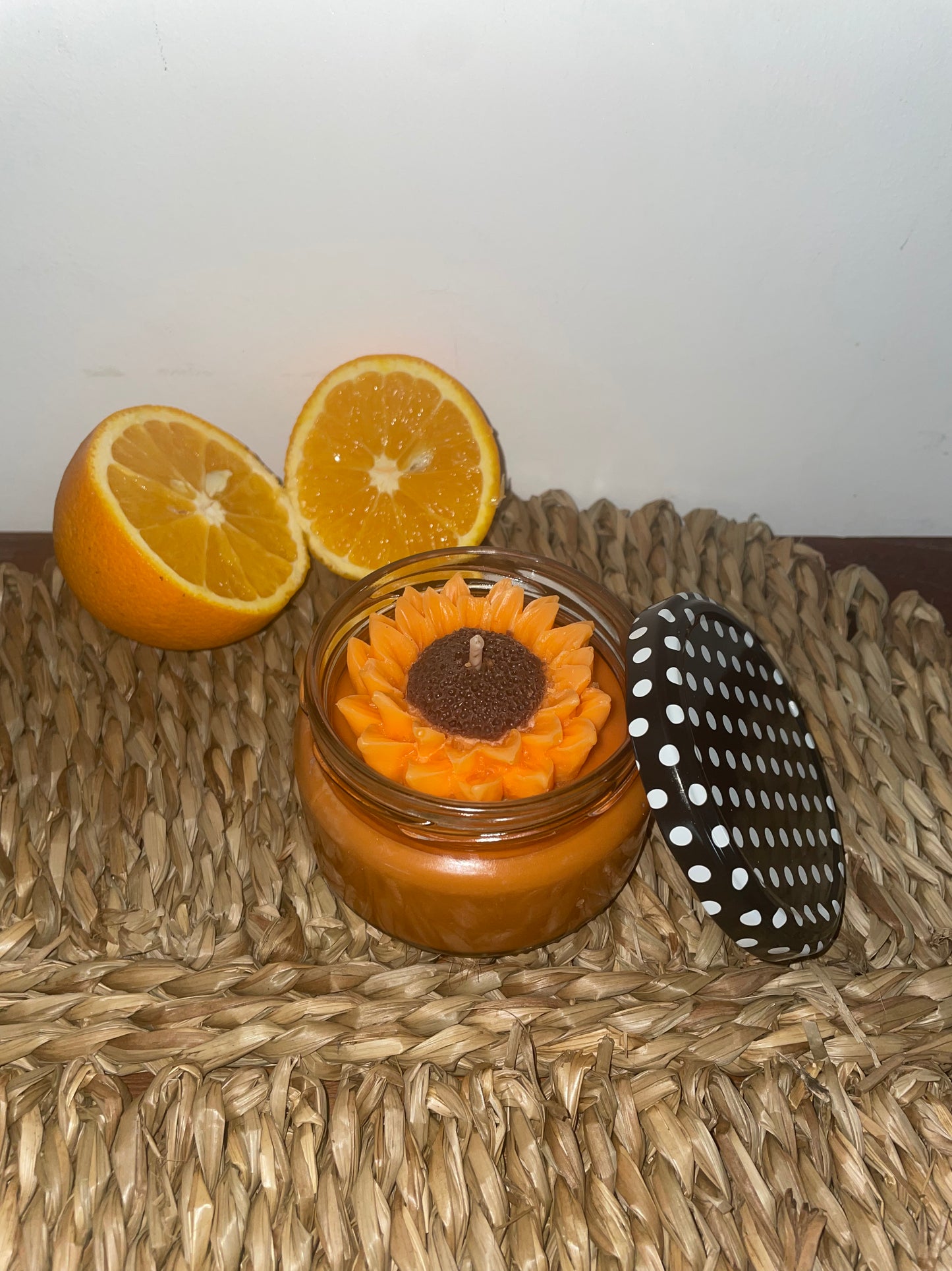Bougie artisanale parfumée fleur tournesol en pot, décorée d’orange, sur tapis naturel