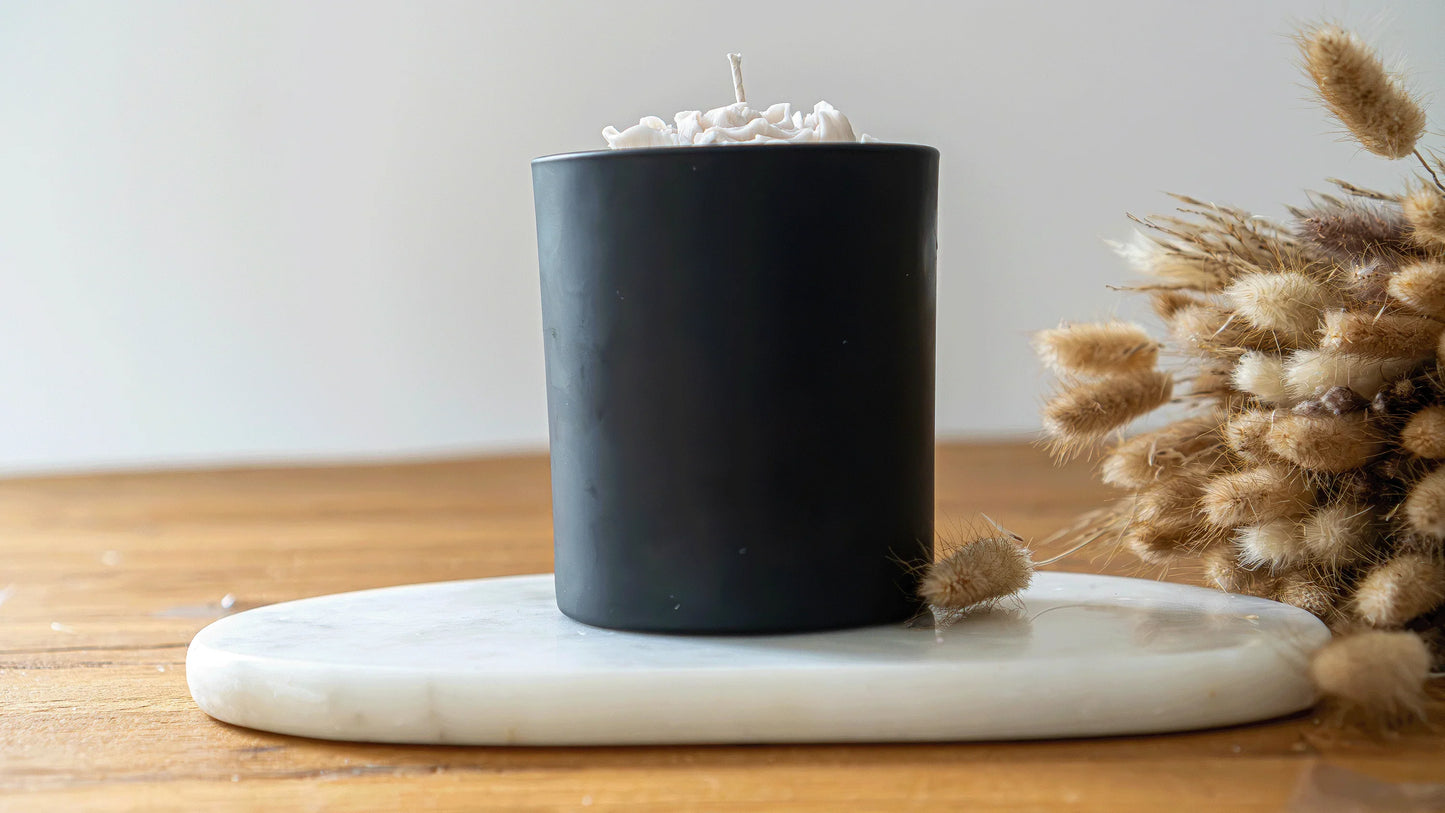Bougie artisanale parfumée noire sur plateau en marbre, fleurs séchées en décor