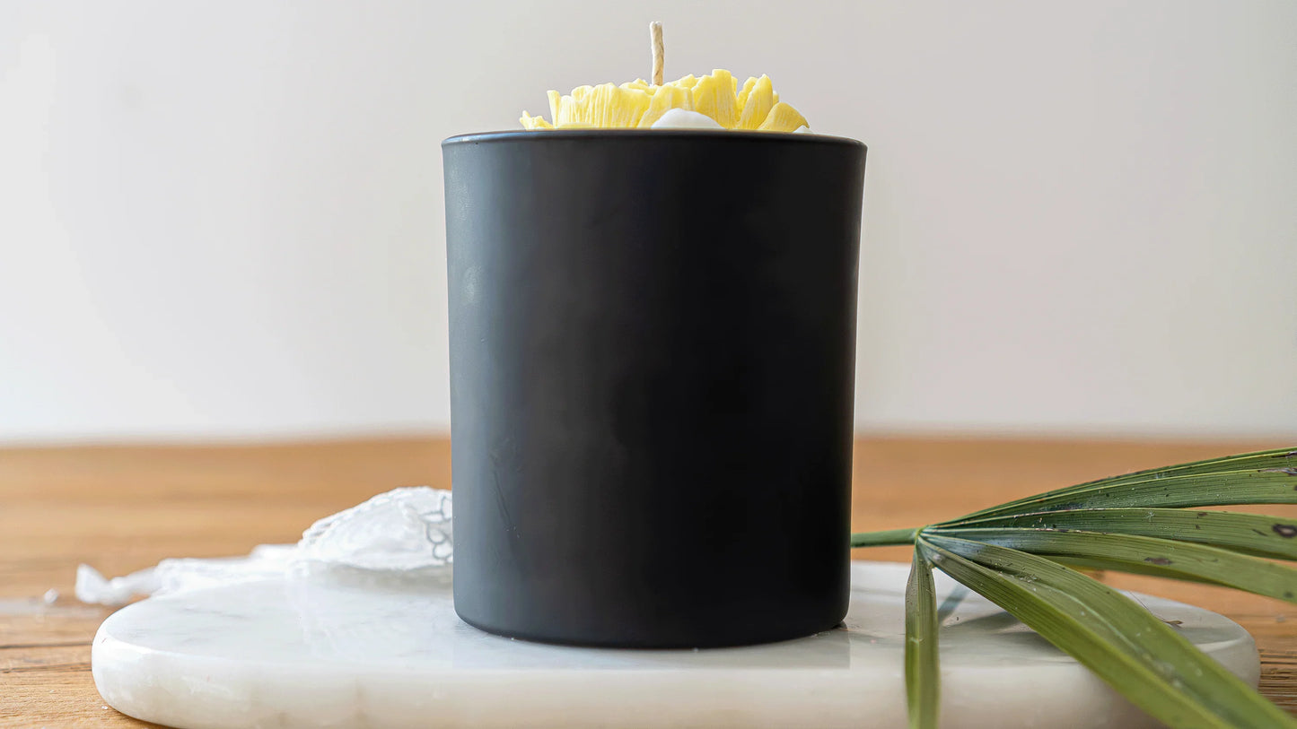 Bougie artisanale parfumée dans pot noir mat, décoration florale, sur plateau en marbre