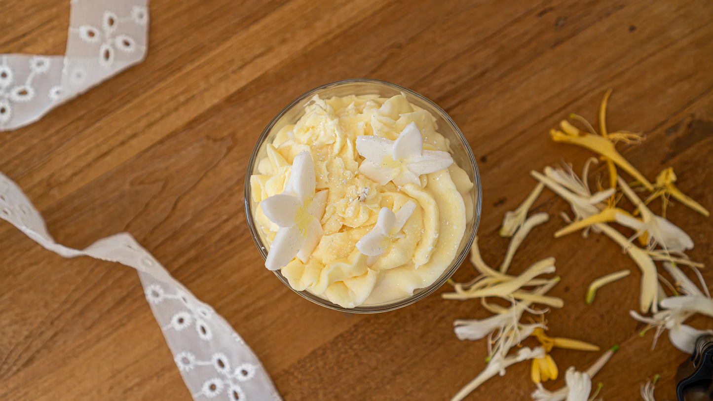 Bougie artisanale parfumée à la fleur, décorée de fleurs blanches, sur table en bois.