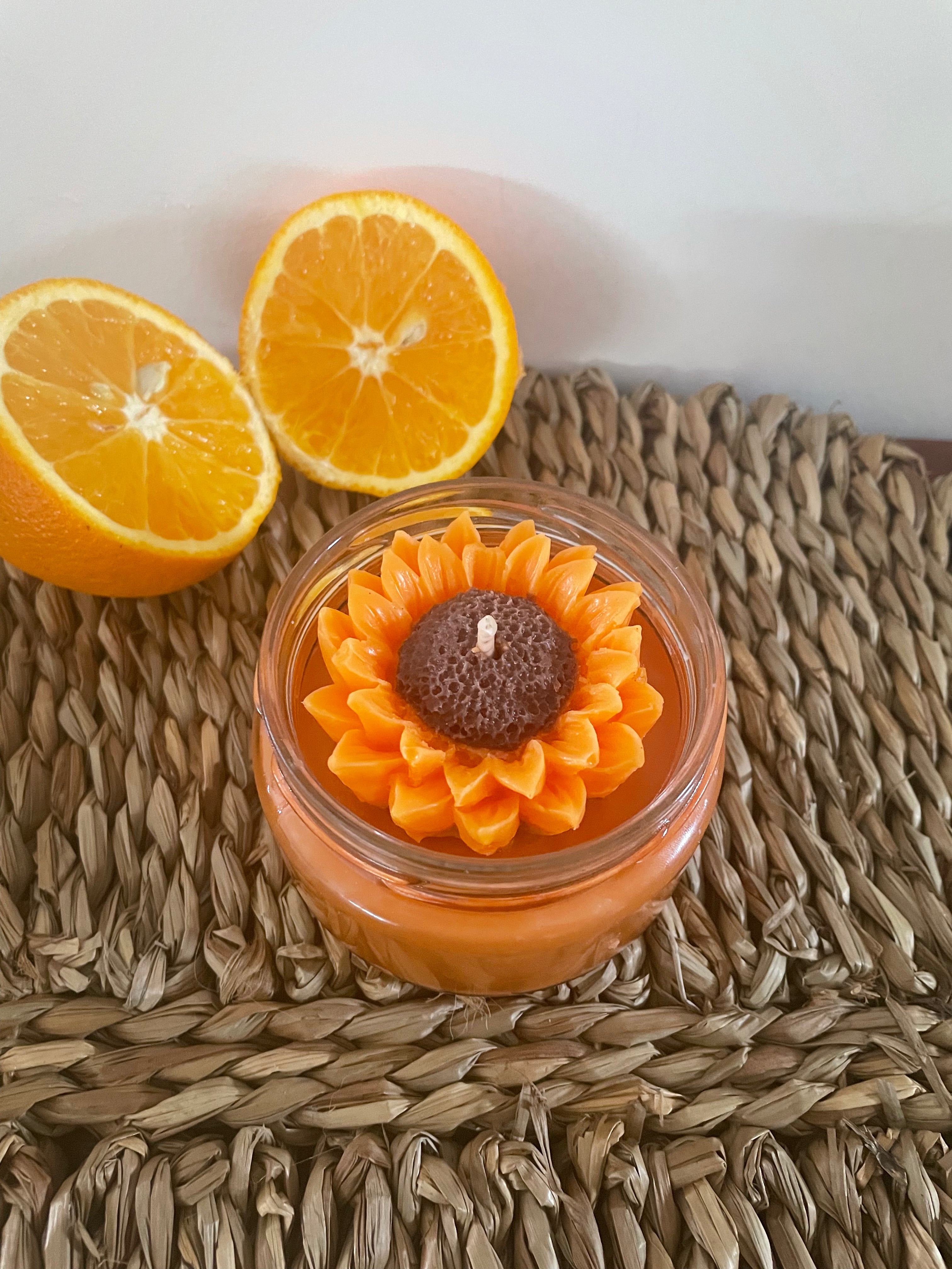 Bougie artisanale parfumée en forme de tournesol, décorée avec des oranges, sur support en rotin.